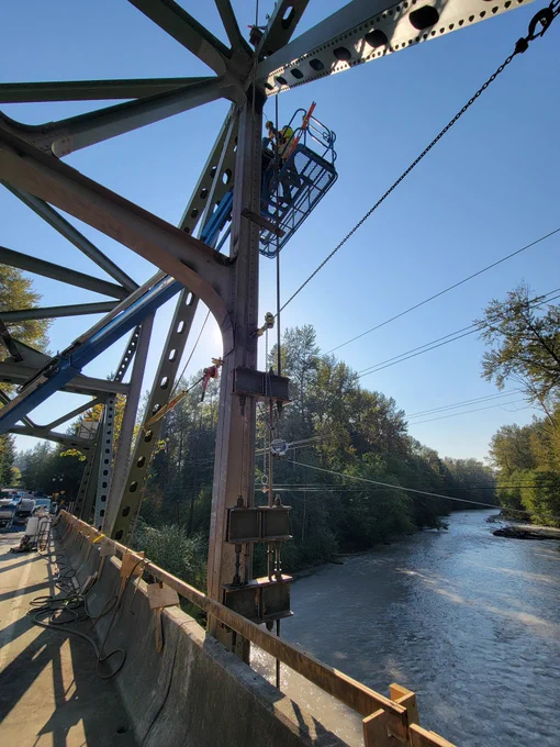 Crews on a lift work on supports of a bridge over a river