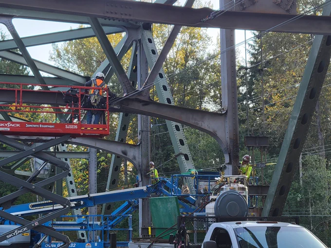 Construction crew on a lift work to straighten steel beams that support a bridge