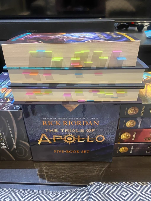 A photo of Mark’s copies of the 15 main books in the Percy Jackson series. Three books are stacked on top with the edges facing outward and there are numerous small Post-It notes poking out.