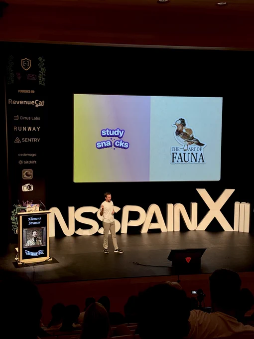 Photo of me on the NSSpain stage. A projector shows two of my app logos (Study Snacks and The Art of Fauna). Underneath is a giant sign saying NSSpain XIII. 