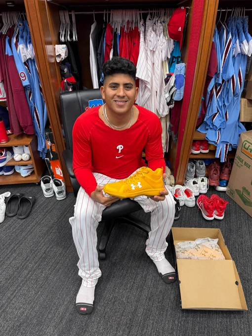 Ranger Suárez smiles and poses for a picture in front of his locker. He's holding an autographed yellow cleat.