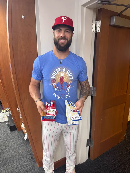 Weston Wilson smiles and holds two pairs of autographed batting gloves in the Phillies clubhouse.