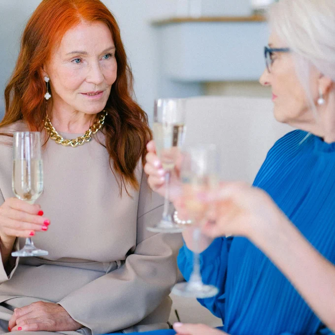 A group of senior women elegantly toasting with champagne glasses indoors.