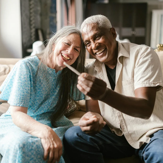Joyful senior couple sharing a joint on a cozy sofa, enjoying their time together.