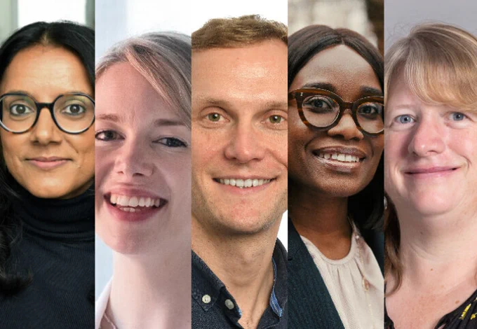 Group portrait of five diverse professionals standing side by side, smiling warmly against a neutral background.