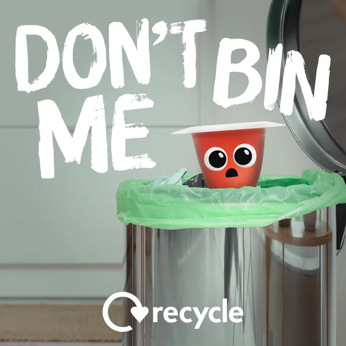 An empty yoghurt pot with a cartoon face in a metal bin