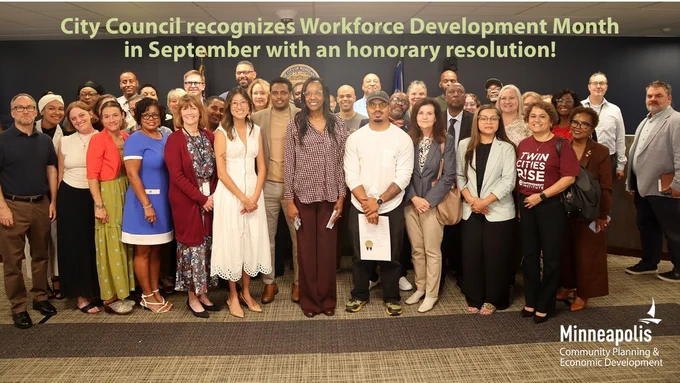 40 people, including Minneapolis City Council members, City staff, Workforce Development Board members, and community partners, stand together in City Council chambers with the honorary Workforce Development Month resolution