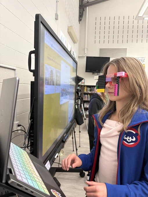 A student standing in the library wearing Lego glasses. 