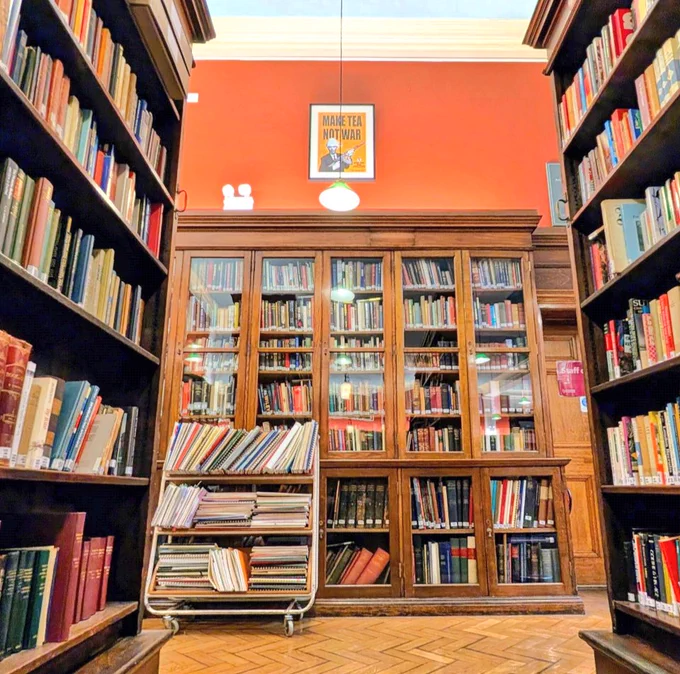 A beautiful old library with wood shelves and red walls. A yellow poster above the shelves says "make tea not war."