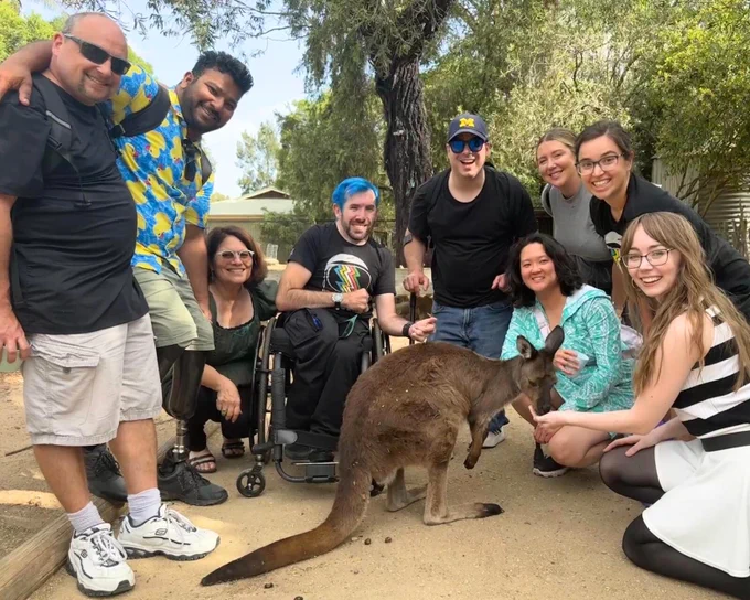 A group of nine members of AstroAccess smiling and posing around a kangaroo in an outdoor setting.