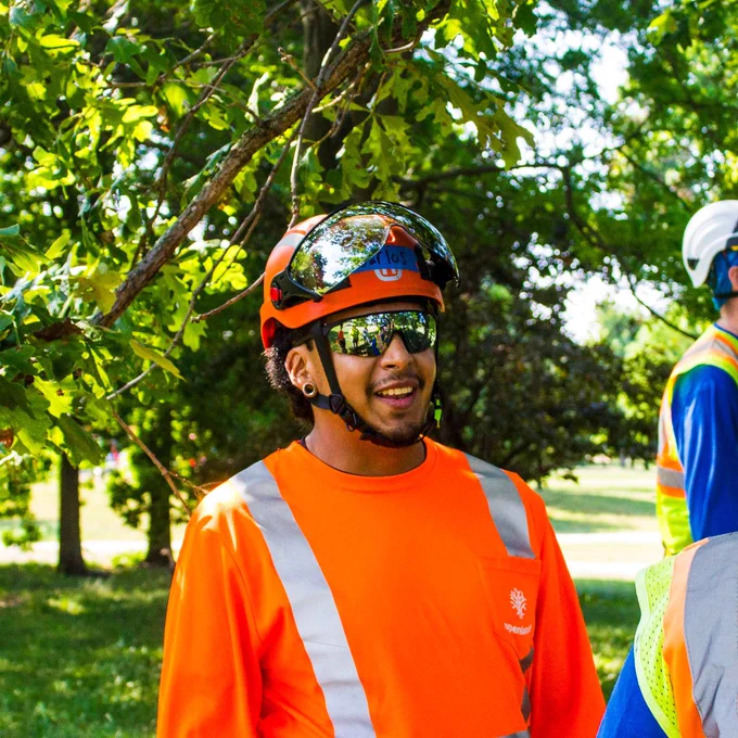 Carlos Ortega, an Openlands employee standing under a tree branch with an orange shirt and helmet.