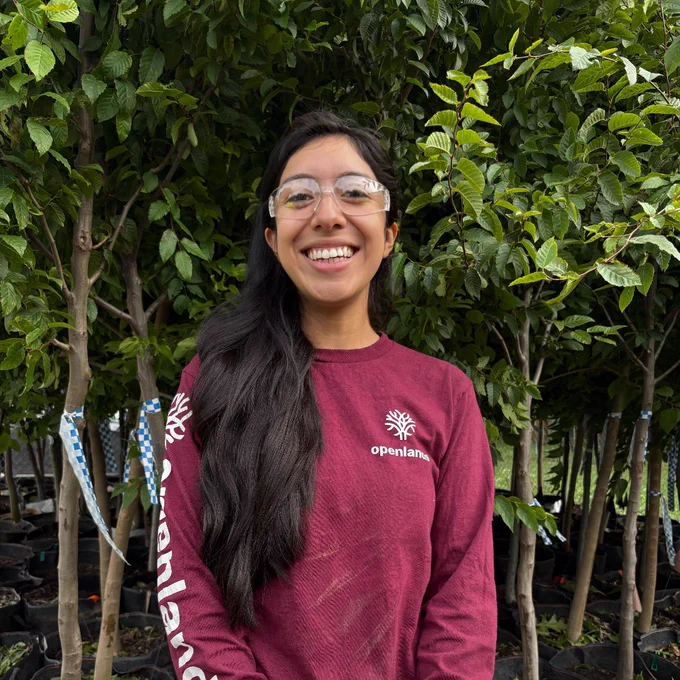 Leslie Leon Aguilar, Openlands' employee with a burgundy shirt and safety glasses standing in front of a tree.