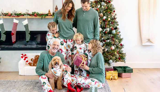 Happy family celebrating Christmas in matching pyjamas couples outfits, sitting by the Christmas tree with gifts and festive decorations.