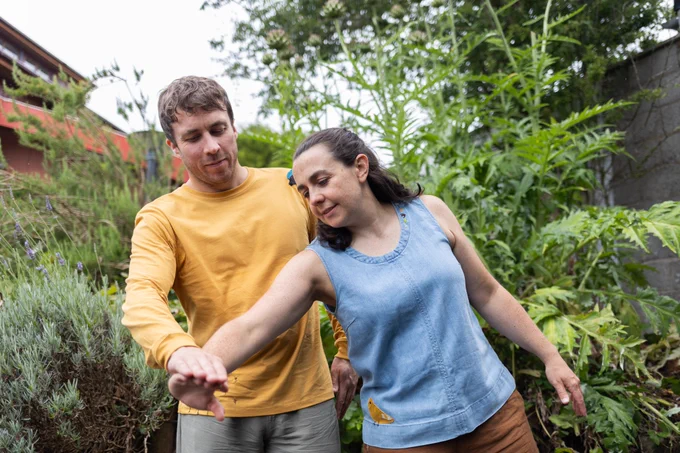 A man in a yellow t-shirt and a woman in a blue vest are dancing together in a garden.