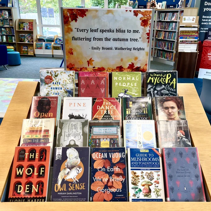 Photograph of an autumnal-themed book display at Ash Library. The display poster features black text on a background with orange and red autumn leaves.  

The text reads:  
"Every leaf speaks bliss to me, fluttering from the autumn tree."  
Emily Bronte, Wuthering Heights 
