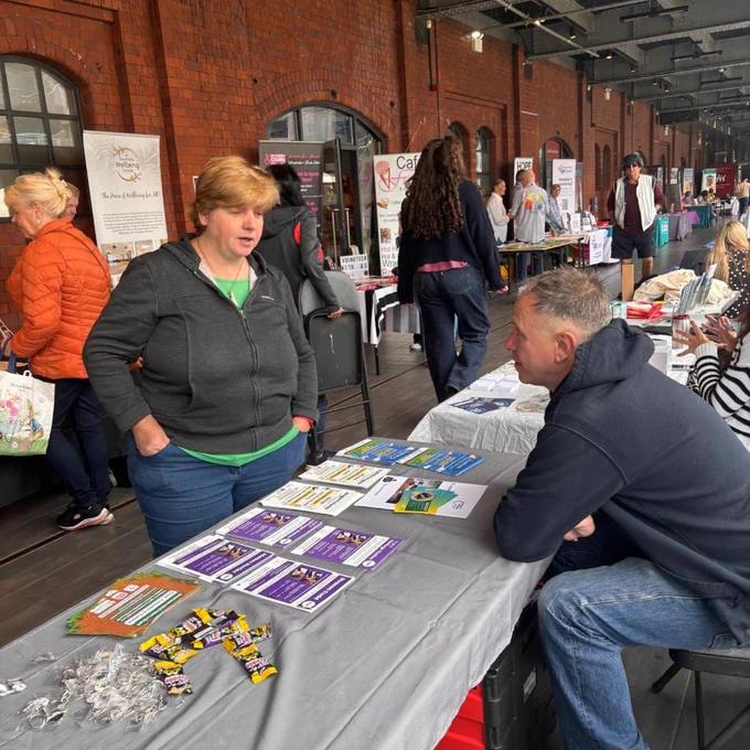 An image of Swansea MAD staff sitting behind a stall in discussion with a person at the National Waterfront Museum.