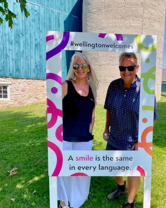 Councillor Diane Ballantyne and Councillor Doug Breen stand behind a cardboad cut out that reads  Wellington Welcomes, A smile is the same in every language.