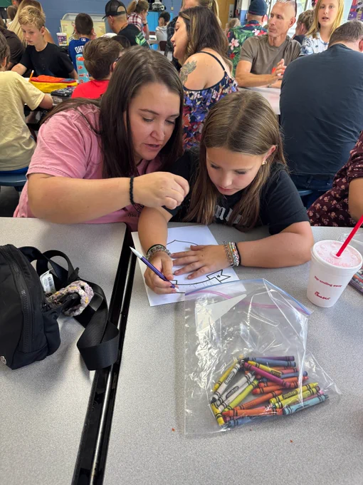mom looks over a fourth graders shoulder as they design their family shield together