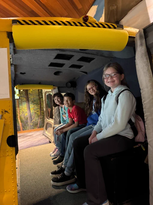 4 students sit in a replica of some kind of big machinery. they are smiling at the camera  