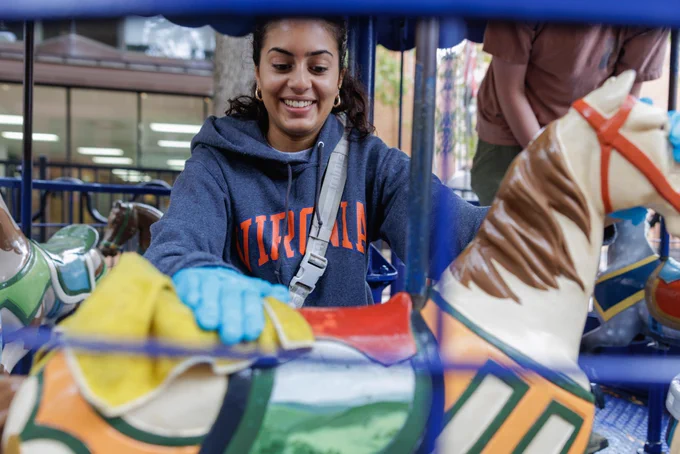 Person in a Universal of Virginia hoodie smiling while riding on a colorful carousel horse.
