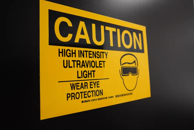 Yellow caution sign warning about high-intensity ultraviolet light, advising to wear eye protection.