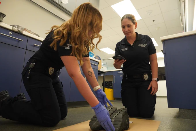 Two crime scene technicians examining and photographing a large shoe impression indoors.