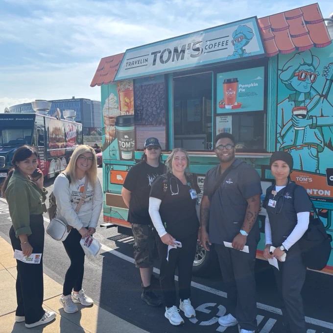 Group of people standing in front of Tom's Coffee food truck on a sunny day.