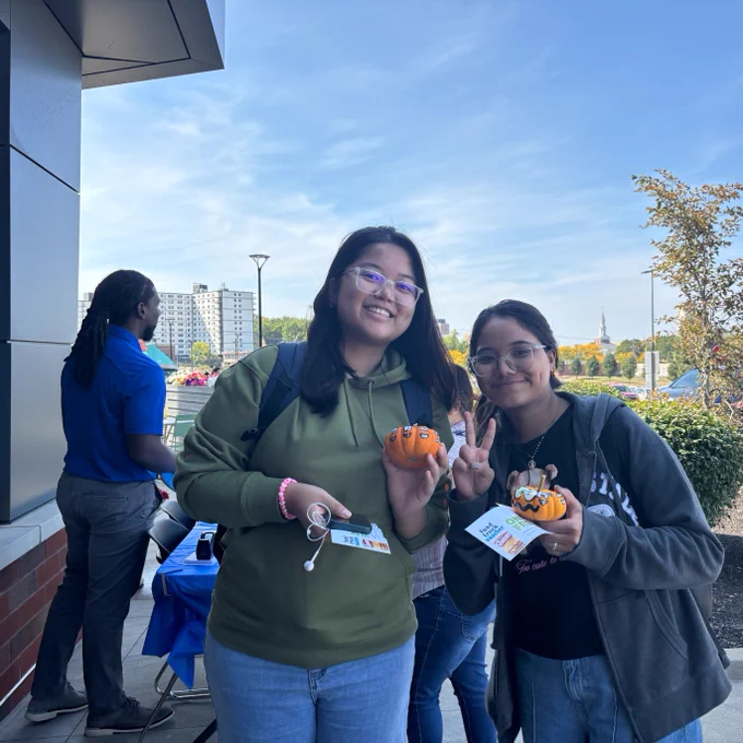 Two individuals smiling and holding decorated pumpkins at an outdoor event at Stark State College.