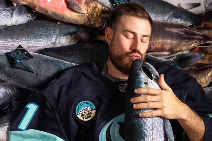 Seattle Kraken goaltender Philipp Grubauer kisses a king salmon plushie while lying in a pile of fish.