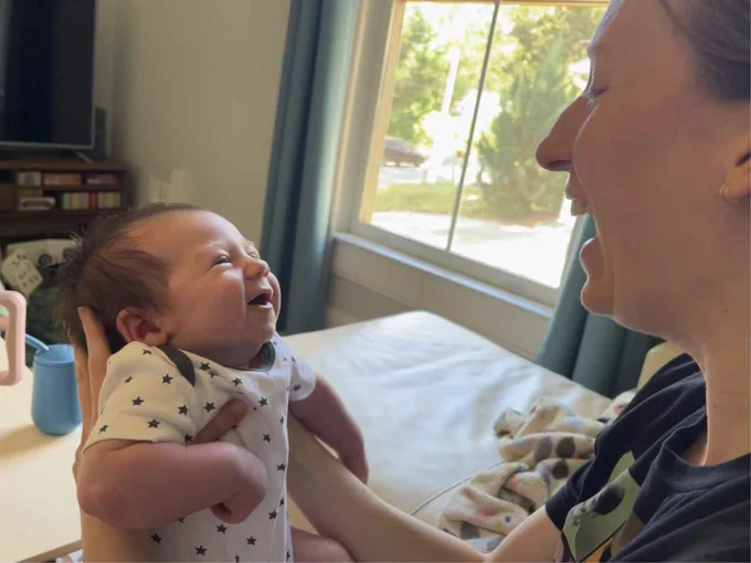 Face to face newborn and woman both with open mouth smiles and eye contact.