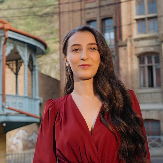 A woman in a red dress stands in front of historic building.
