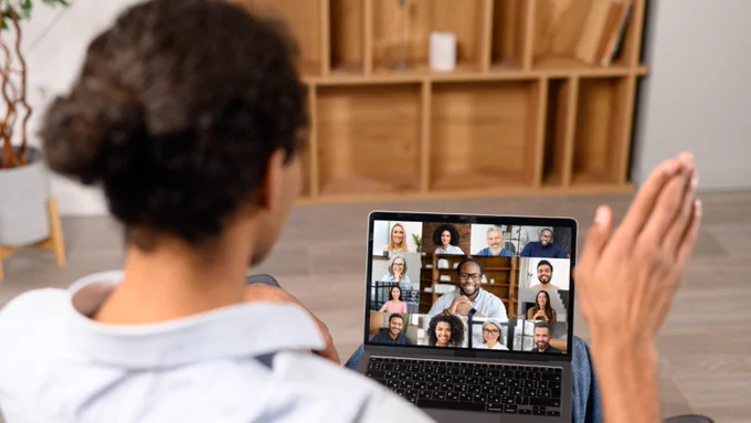 Person participating in a virtual meeting on a laptop with multiple colleagues visible on screen in a grid layout.