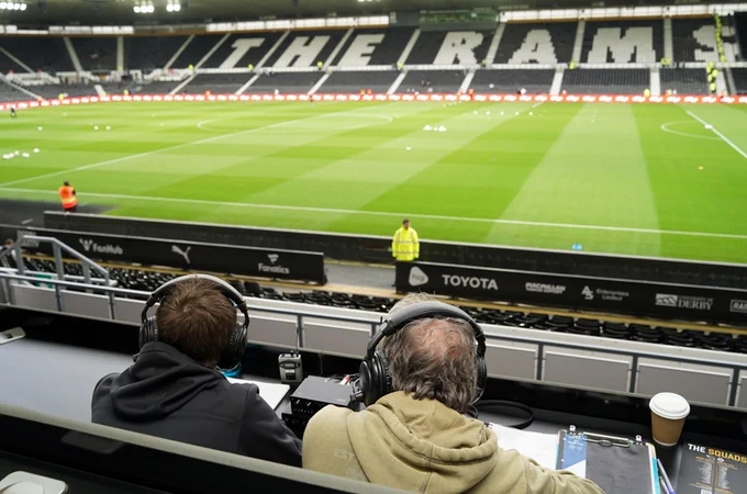 Two members of Derby County's audio descriptive commentary team providing live match coverage from their position on the press bench at Pride Park Stadium, overlooking the pitch.
