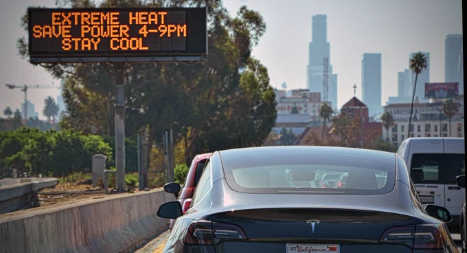 A Tesla electric car is driven past a sign warning of extreme heat and the need to save power between 4-9pm. Los Angeles, USA. September 2022. Mandatory Credit: Chris Yarzab