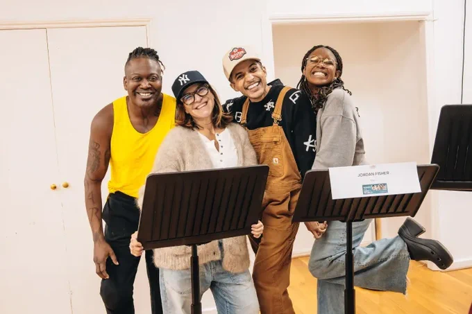 Tituss Burgess, Shoshana Bean, Jordan Fisher, and Joy Woods smile together in a rehearsal room 