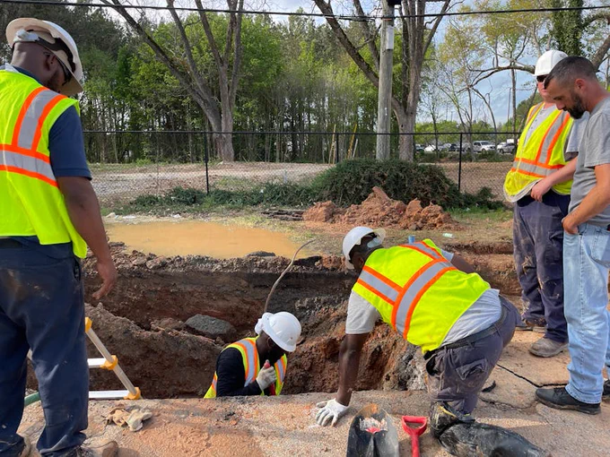 Team of construction workers inspecting an underground utility site on a sunny day.