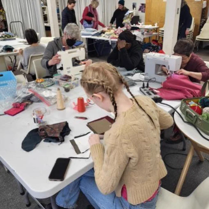 The community group, Works-in-Progress, hosts a repair workshop. Someone works at a sewing machine. 