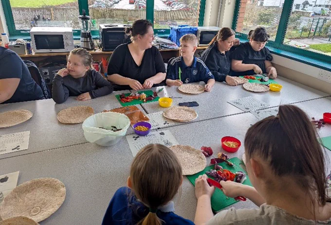 Pupils and teachers working with food, sat at a large table.