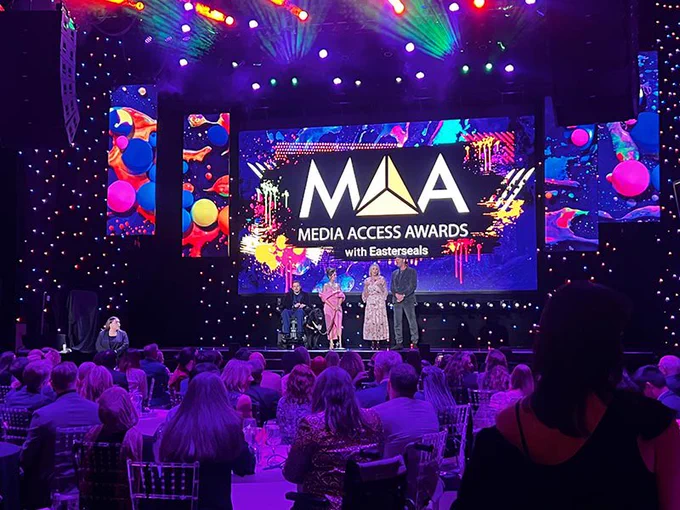[1-4 - A series of photos of individuals who were honored by the Media Access Awards virtually and on stage in 2023 and 2024, featuring Deborah Calla, Allen Rucker, Sofia Sanchez, and Troy Kotsur. In the background of photos 1 and 2, is a large screen on-stage featuring the MAA logo].