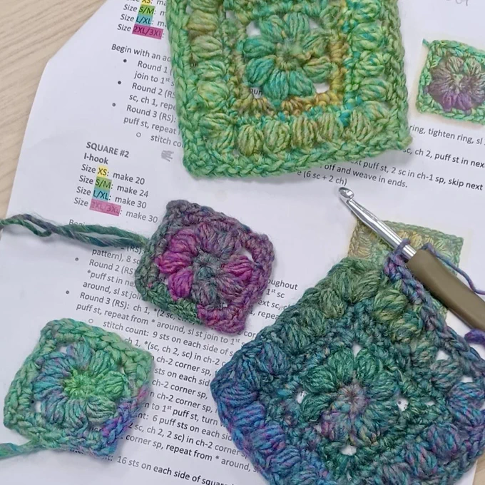 Colourful crocheted granny squares in different sizes, laid on top of a crochet pattern.