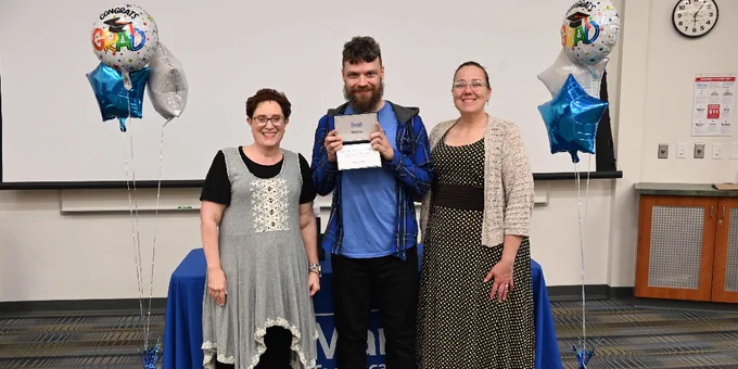 A graduate holds his diploma next to his instructors. 