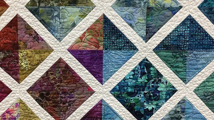 A closeup of a latticework quilt with floral patterns in shades of purple and blue.