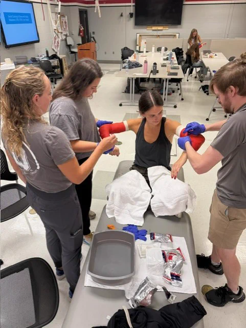 4 third year ot students practicing casting in lab. One student is getting both arms casted by the other 3 students