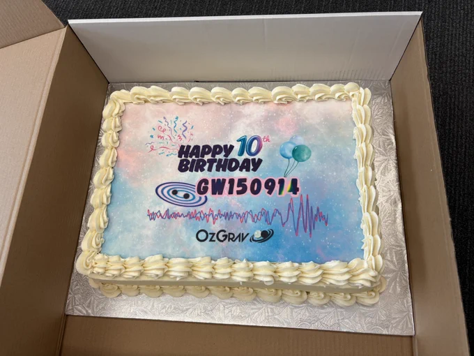 A sheet cake decorated with "Happy 10 Birthday GW150914", confetti, balloons, a binary black hole, and the data from our first detection, as well as the OzGrav logo. It is edged with some creamy frosting.