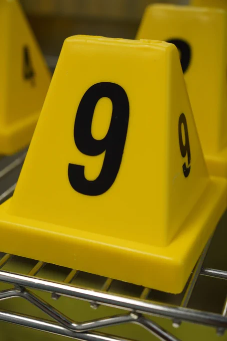 Close-up of a yellow plastic evidence marker labeled with the number 9 in bold black print, sitting on a metal shelf.