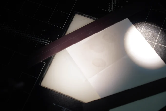 A light shining on a piece of white paper with faint fingerprints on them.