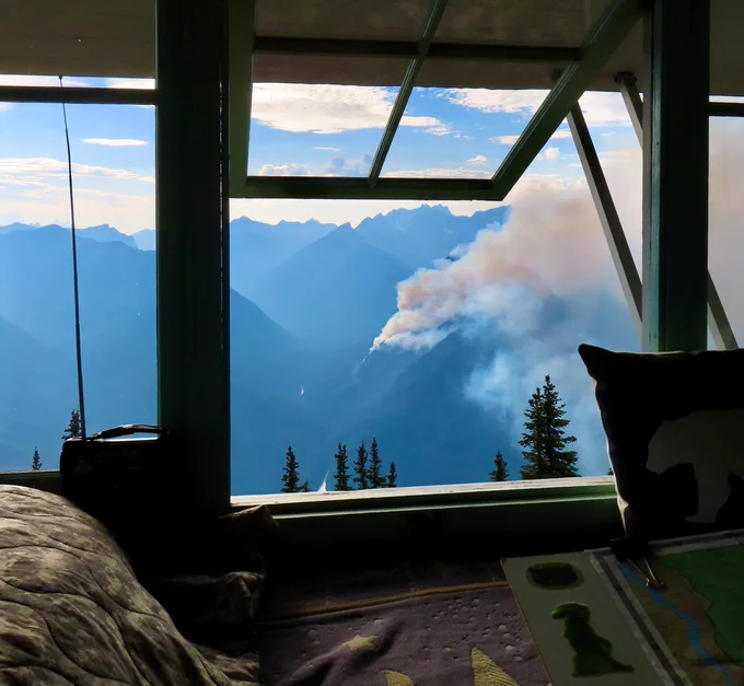 Smoke from a forest fire burning on distant peaks is seen through a fire lookout window.