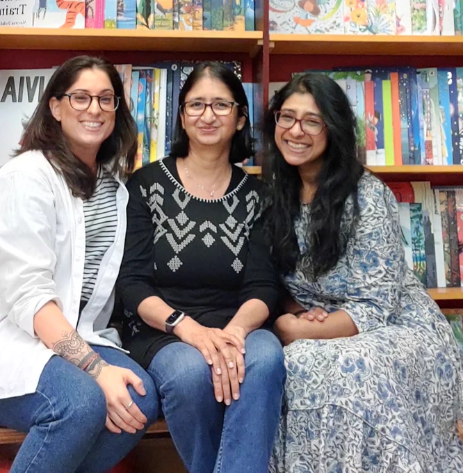 SAILfest co-founders Sinead Gosai, Chitra Soundar and Sanchita Basu De Sarkar are pictured sitting together smiling in front of bookshelves.