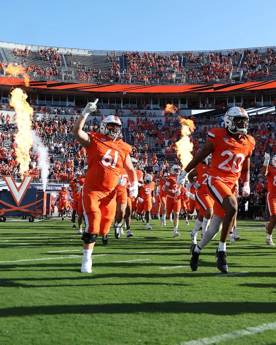 University of Virginia football players running onto the field with celebratory flames erupting in the background at Scott Stadium.
