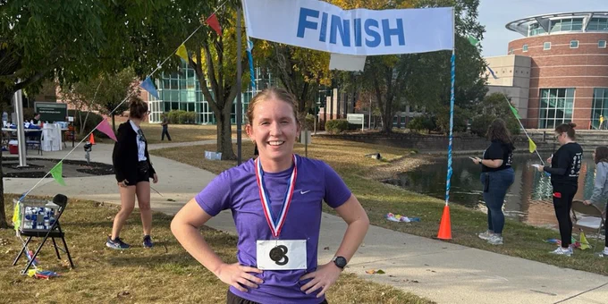 A woman poses with her medal in front of the finish line.